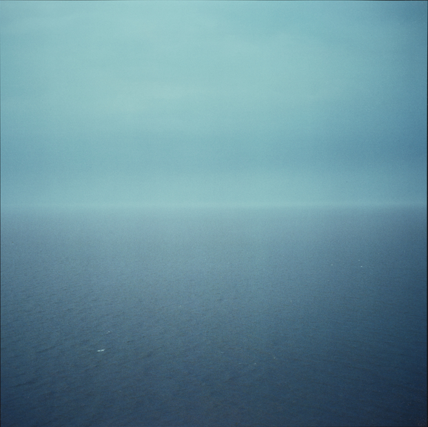 A square photograph with the line where the sea meets the horizon in the centre of the image. The photograph shows a view of Wales from Bristol. The sky and the sea are a beautiful, deep colour blue